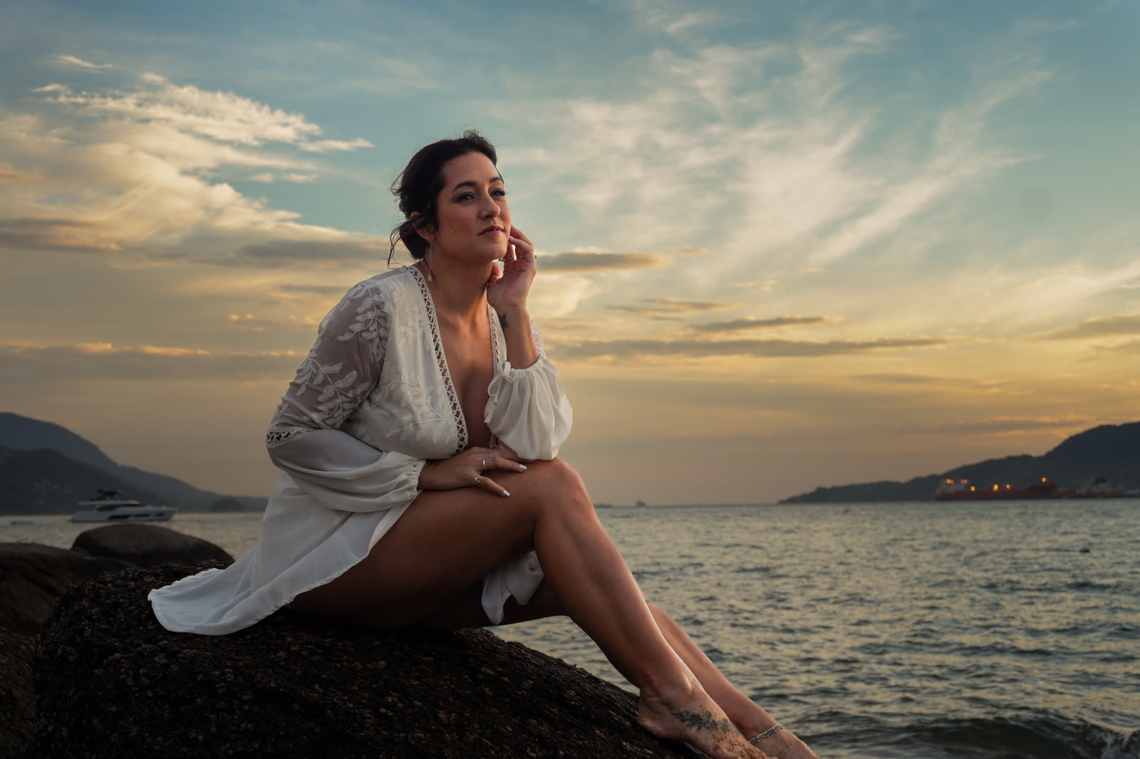 Noiva sentada na pedra, de frente para o mar, no fim da tarde