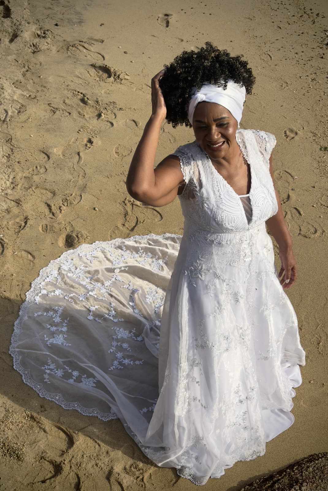 Noiva deitada na areia, vestido de renda espalhado e turbante branco