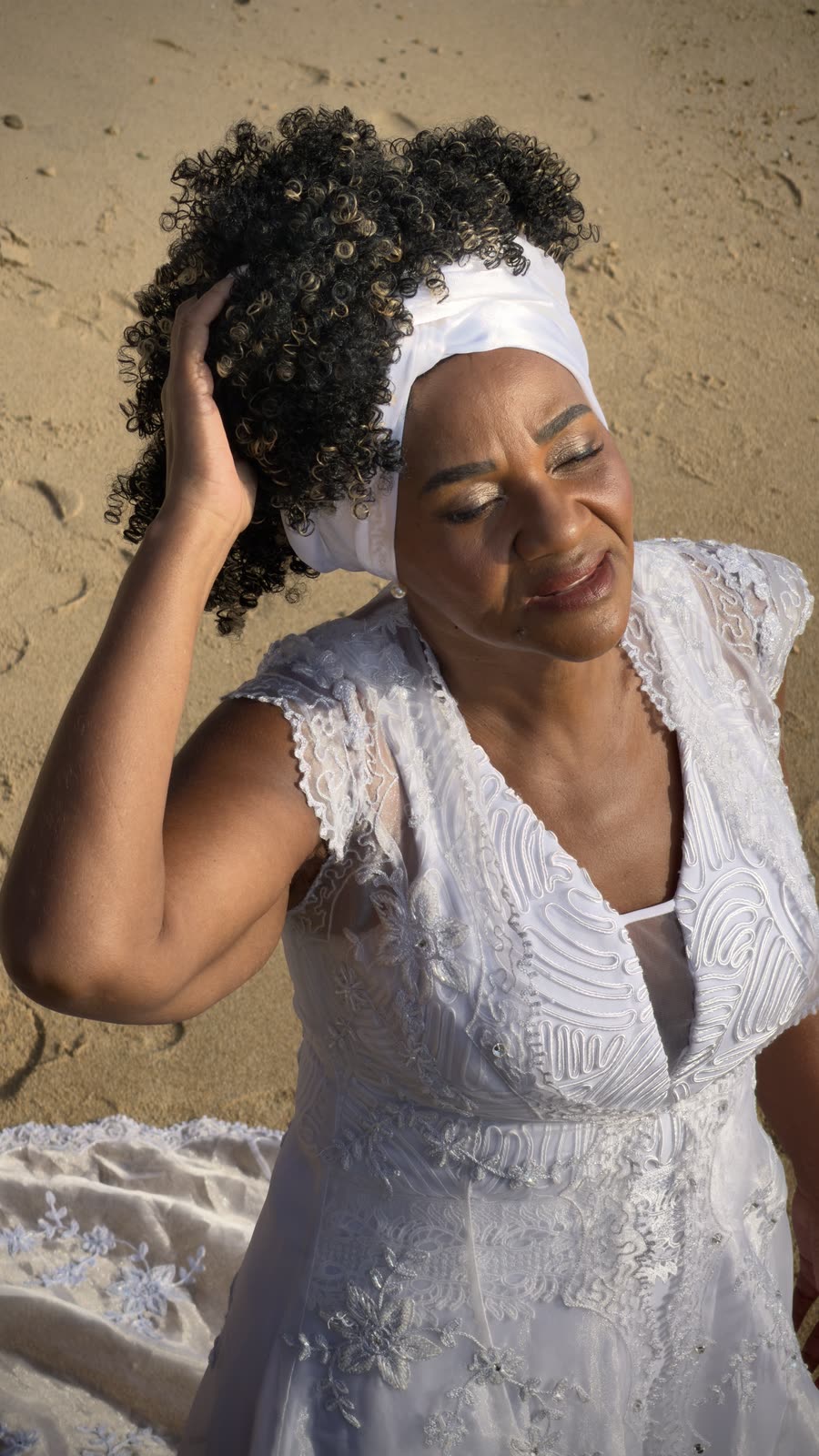 Retrato da noiva na areia, sorrindo com a mão no cabelo